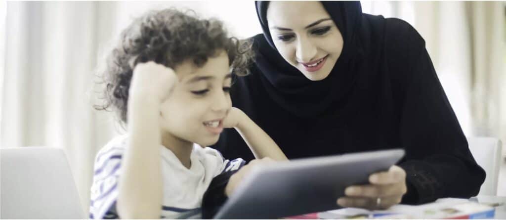 A woman in a hijab is helping a small child with an iPad